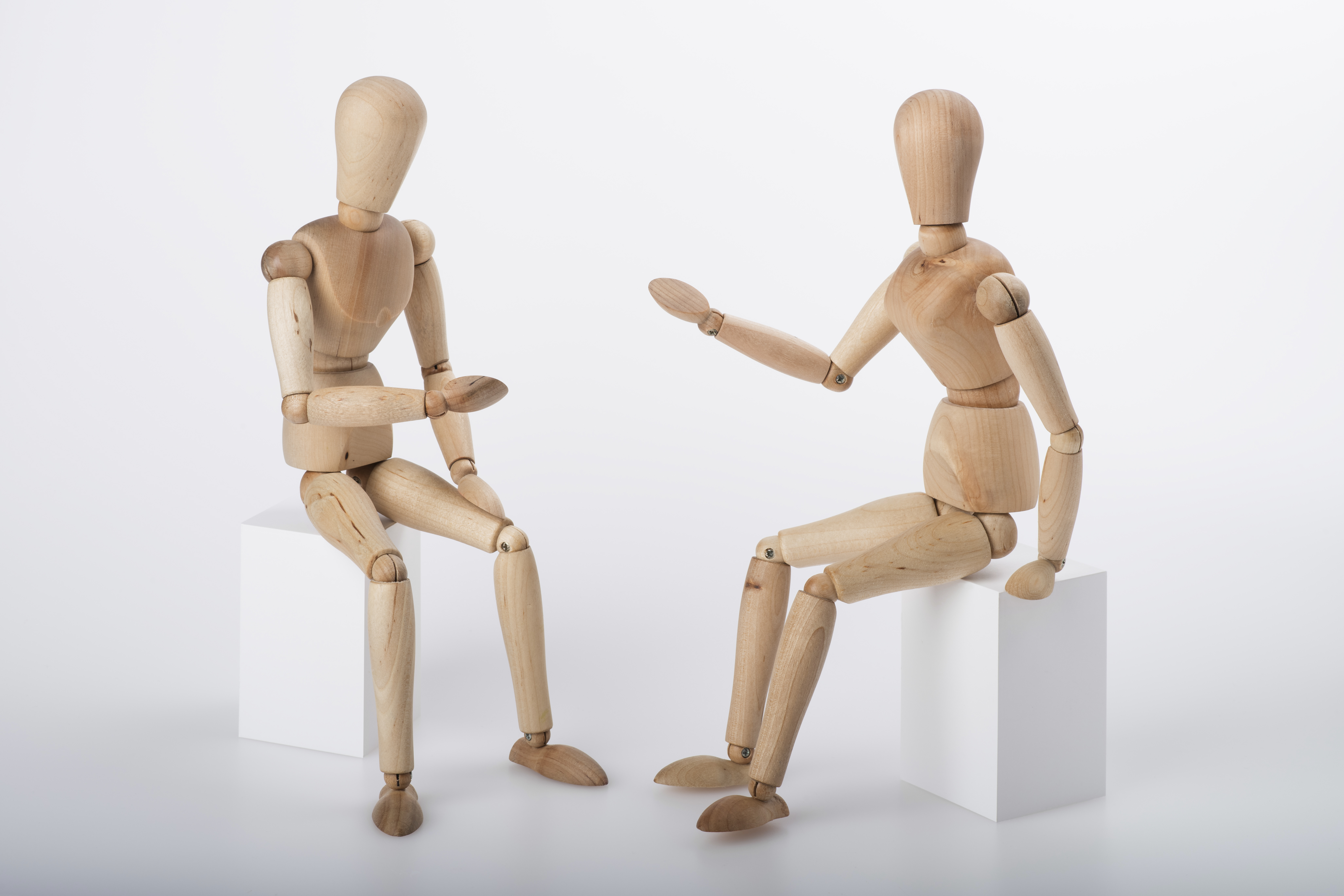 Zwei Figuren aus Naturholz mit verstellbaren Gliedern sitzen sich in einer diskutierenden Haltung gegenüber